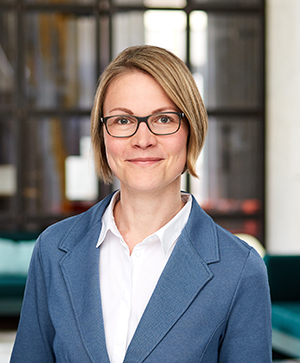 Portrait der Koordinatorin Innovationsteam & AGs Dr. Anna Leipprand. Im Hintergrund sind eine große Glasfront sowie zwei dunkelgrüne Sofas zu sehen.