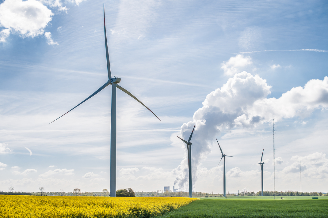 Windräder auf einem weiten Feld, am Horizont eine Industrielandschaft