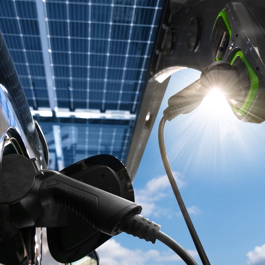 Nahaufnahme eines Elektroautos, das an einer Ladestation mit Solarpanelen im Hintergrund aufgeladen wird.
